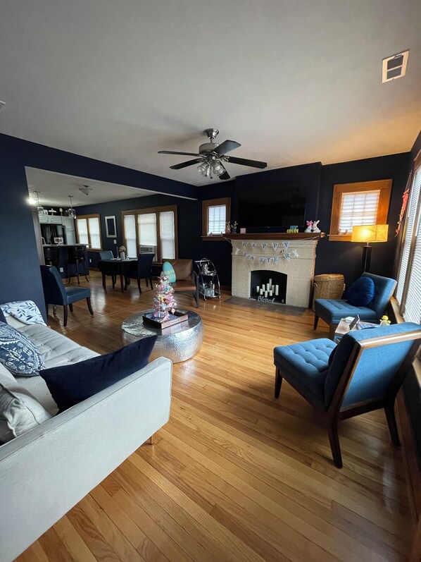 A living room with a fireplace, a dining area, and a kitchen in the background.