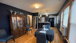 Uma sala de jantar com uma mesa posta para quatro pessoas, rodeada por cadeiras, e um armário de madeira com portas de vidro.