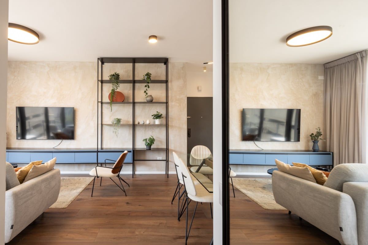 Een moderne woonkamer met een bank, stoelen, een televisie en een plantenplank.