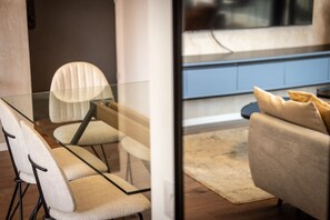 A modern interior with a glass table surrounded by chairs, a sofa with cushions, and a view through a glass partition.