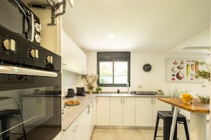 A modern kitchen with white cabinets, a built-in oven, a coffee machine, and a window with a view.