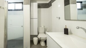 A modern bathroom with a glass shower enclosure, a toilet, and a sink with a mirror above. - Modern 2BR Apartment Near Baháʼí Gardens – Haifa (Haifa)