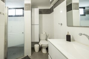 Un bagno moderno con cabina doccia in vetro, un water e un lavandino con specchio sopra.