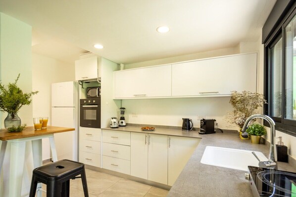 A modern kitchen with white cabinets, a built-in oven, a coffee maker, and a sink.