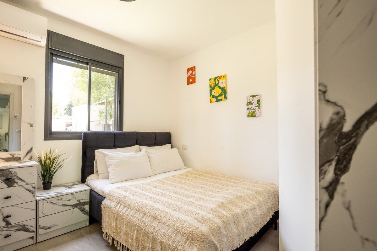 A bedroom with a bed, a nightstand, a dresser, a window, and wall art.