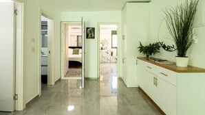 A hallway with a white cabinet, a potted plant, and a door leading to a room. - Modern 2BR Apartment Near Baháʼí Gardens – Haifa (Haifa)