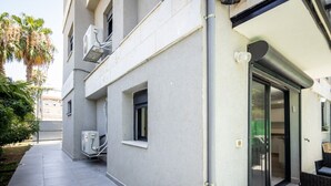 A building with a covered outdoor seating area, air conditioning units, and a sliding glass door leading to an interior space. - Modern 2BR Apartment Near Baháʼí Gardens – Haifa (Haifa)