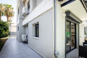 Un edificio con una zona salotto esterna coperta, condizionatori d'aria e una porta scorrevole in vetro che dà su un ambiente interno.
