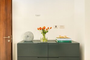 Een kamer met een houten deur, een grijs dressoir, een vaas met oranje bloemen en een boek getiteld 'A Century of Israeli Art'.
