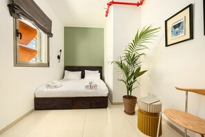 Une chambre à coucher avec un lit, une plante en pot, une chaise, une petite table et un tableau encadré accroché au mur.