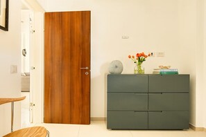 Une pièce avec une porte en bois, un meuble gris orné d’objets décoratifs et une petite table sur laquelle est posé un vase de fleurs.