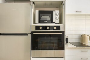 Een kleine keuken met een inbouwoven, een magnetron en een koelkast.