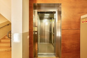 Un ascenseur avec un intérieur métallique, une barre de maintien et un mur en bois situé à côté.