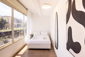 Een slaapkamer met een groot raam, een bed met opgerolde handdoeken en abstracte wanddecoratie.