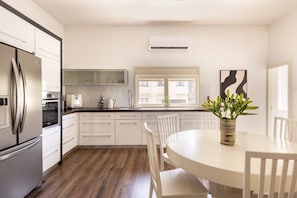 Een moderne keuken met witte kasten, een roestvrijstalen koelkast, een inbouwoven, een magnetron, en een raam voor natuurlijk licht.
