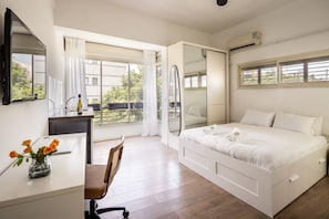 A bedroom with a bed, a desk, a chair, a mirror, and a window. - Sunlit Oasis • Heart of the City by SeaNRent (Tel Aviv)
