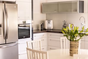 Een moderne keuken met een koelkast, oven, broodrooster en een potplant op de tafel.
