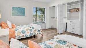 Een slaapkamer met twee bedden, een kast en een raam met jaloezieën.