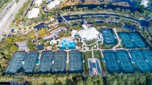 An aerial view of a resort with multiple tennis courts, a swimming pool, and a large building with a unique roof structure. - -Sunny Naples Charm-Your Perfect Naples Getaway! (Naples)