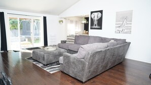 Un soggiorno moderno con un divano grigio, un pouf abbinato e un cuscino decorativo a righe. Alle pareti, due quadri con immagini di animali.