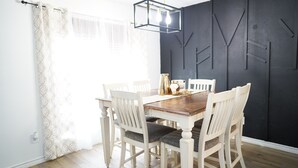 Zona pranzo con tavolo in legno e sedie bianche, parete di contrasto scura e tenda a motivi geometrici.