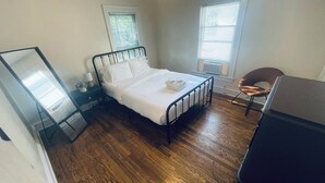 Ein Schlafzimmer mit Bett, Stuhl, Schreibtisch und zwei Fenstern.