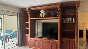Una sala de estar con un televisor de pantalla plana grande, armarios de madera y una pequeña decoración en la repisa.