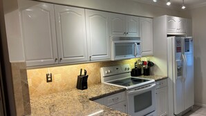 Una cocina con gabinetes blancos, encimera de granito, microondas, horno y refrigerador.