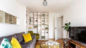 Un salon moderne avec un canapé gris, des coussins jaunes, une table basse en verre et un meuble TV en bois.