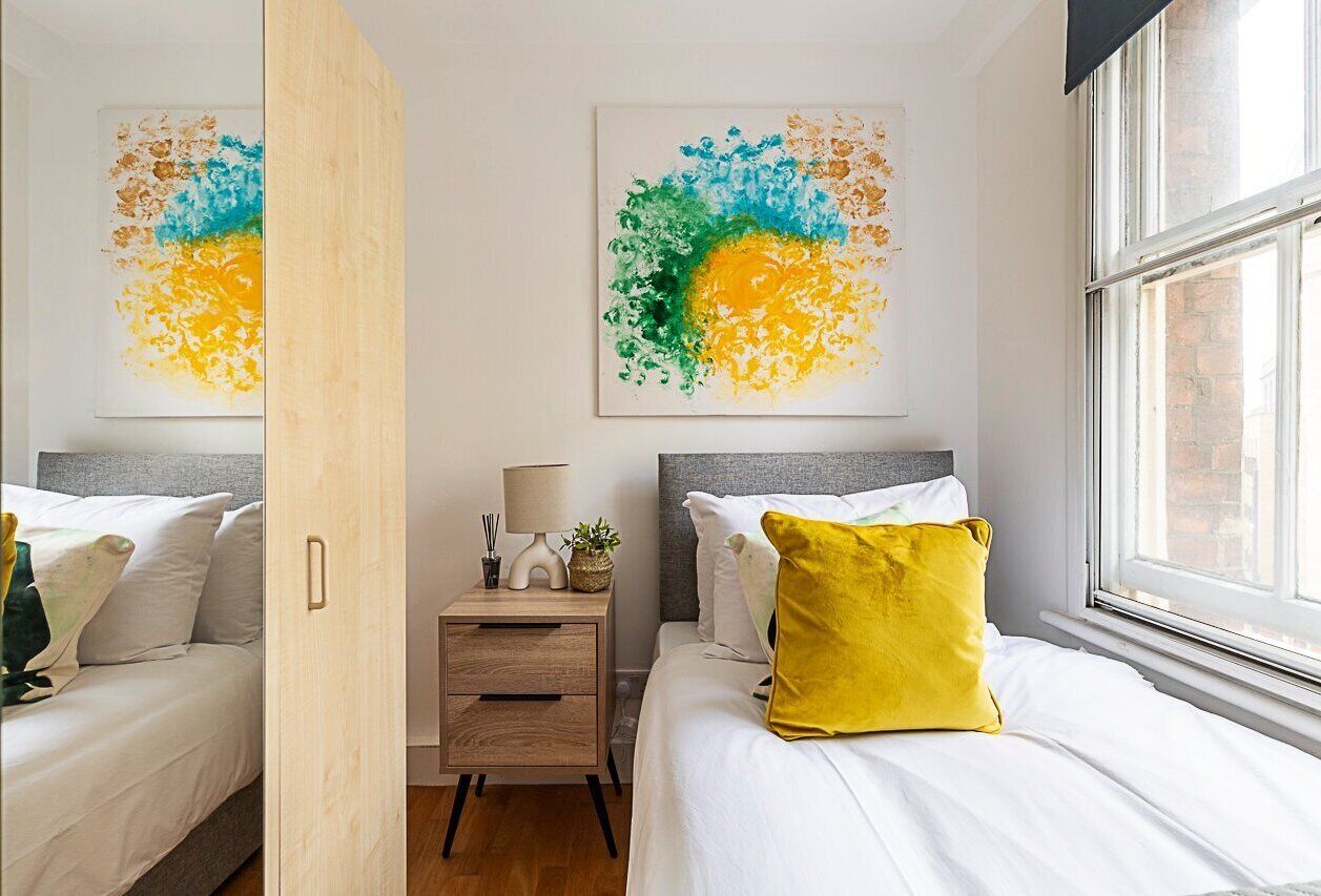 A modern bedroom with two beds, a nightstand, and abstract art on the walls.