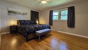 A bedroom with a bed, a bench, a ceiling fan, a nightstand, and a window with curtains. - Rockford Cascade Getaway (Rockford)
