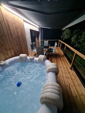 En utomhusbubbelpool med ett trädäck och ett bord med stolar.