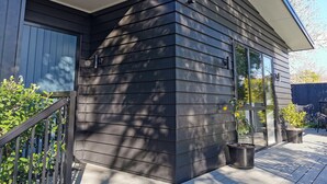 Una casa moderna con revestimiento oscuro, una puerta de garaje visible y un pequeño porche con plantas en macetas.
