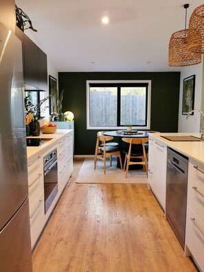 Una cocina con armarios de madera, una mesa de comedor con sillas, un ventanal y una lámpara colgante.