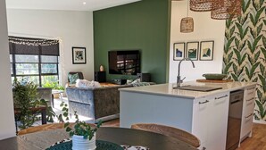 Una cocina moderna con una isla central, un comedor con mesa redonda y una sala de estar con sofá y televisor.