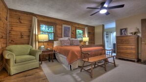 Una habitación acogedora con una cama, un sillón verde, un banco de madera, un aparador y un ventilador de techo.