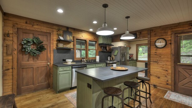 Una cocina con paredes de madera, una isla central con taburetes y un colgante.
