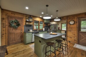 A kitchen with wooden walls, a central island with stools, and a hanging light fixture.
