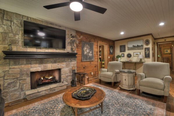 A cozy living room with a stone fireplace, comfortable seating, and a television mounted above it.