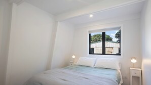 Et soveværelse med en enkeltseng, to sengeborde, et vindue med udsigt til en udendørs bygning, og en loftlampe.