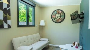 Une pièce avec un canapé beige, une horloge murale ronde, une lampe et une petite table sur laquelle se trouve un vase.