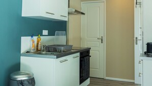 Une cuisine de taille réduite avec des meubles blancs, un évier en acier inoxydable et une poubelle.