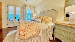 Ein Schlafzimmer mit Bett, Kommode, Deckenventilator und Blick durch das Fenster.