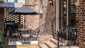 A patio with a grill, outdoor table, and chairs, adjacent to a brick building with a staircase and a door. - The Reed Retreat, 4BR Luxe by Velvet Ditch Villas (Oxford)