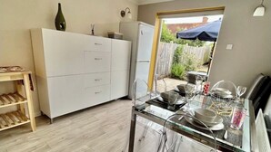 Een moderne keuken met een glazen eettafel, witte kastjes en een koelkast.