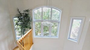 Una habitació àmplia amb escala de fusta, finestres grans i un penjador.