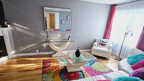 Un saló modern amb un sofà blanc, coixins decoratius de colors, una taula de centre de vidre i un paviment de fusta.