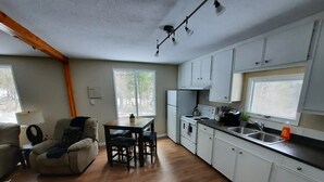 A compact kitchen with white cabinets, a dining area with a table and chairs, and a window providing natural light. - Cozy 3 bedroom cottage in the woods

 (Salmon Arm)
