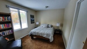 A bedroom with a bed, two bedside tables with lamps, a bookshelf, and a window. - Cozy 3 bedroom cottage in the woods

 (Salmon Arm)