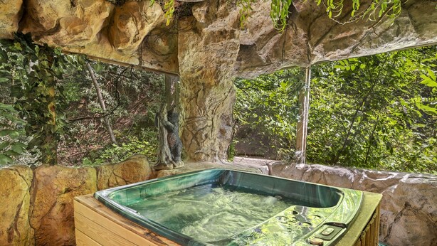Una vasca idromassaggio in un ambiente naturale, con pareti rocciose e vista sul verde.